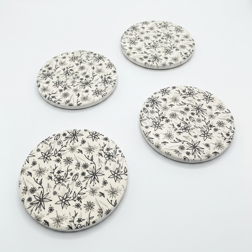 Four round ceramic coasters with floral pattern on a white background