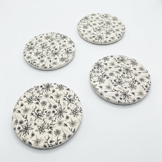 Four round ceramic coasters with floral pattern on a white background